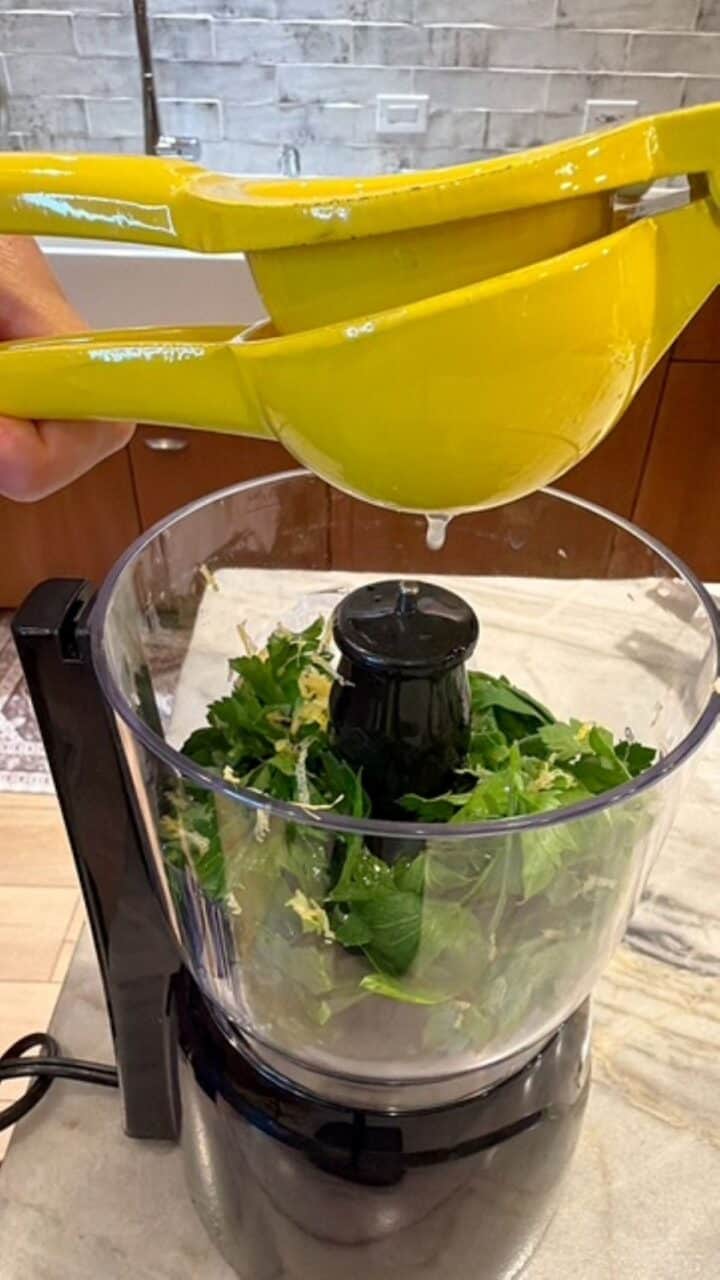 Squeezing lemon juice into a mini-food processor with parsley and ingredients for lemon-parsley sauce.