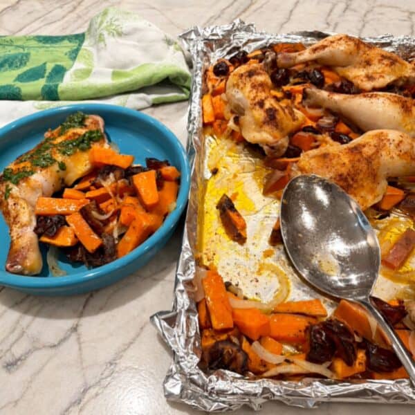 Chicken legs with roasted sweet potatoes and vegetables on a baking sheet and plate.