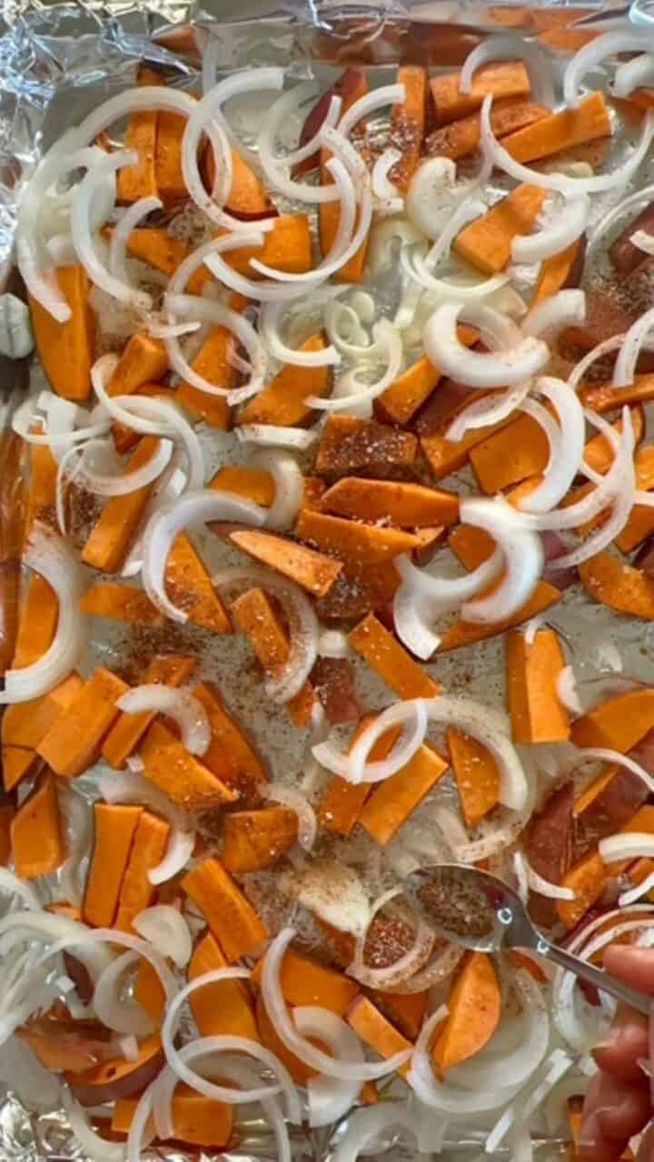 Seasoned sweet potatoes and onions on a baking sheet.